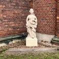 Skulptur "Justitia" Skulptur der Justitia aus Stein mit Schwert und Waage vor einer roten Backsteinmauer.