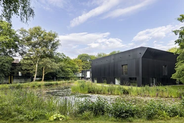 Modernes schwarzes Museumsgebäude am Teich, umgeben von Grünflächen und hohen Bäumen.