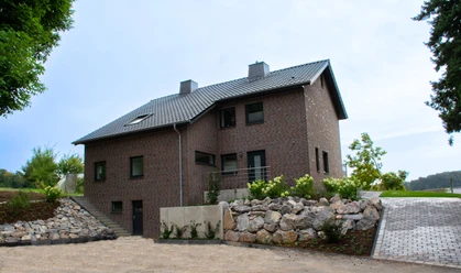 Ferienhaus Blankenrode Zweistöckiges Backsteinhaus mit grauem Dach, umgeben von gepflegter Natur und Blumenbeeten.