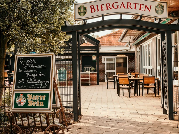 schneiders am Museumshof Biergarten.jpg Eingang zu einem Biergarten mit Schild und Sitzbereich unter freiem Himmel, einladende Atmosphäre.