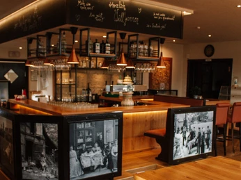 Schneiders am Museumshof.jpg Einladendes Restaurant mit Holzbar, charmante Schwarzweiß-Fotos und gemütliche Beleuchtung.