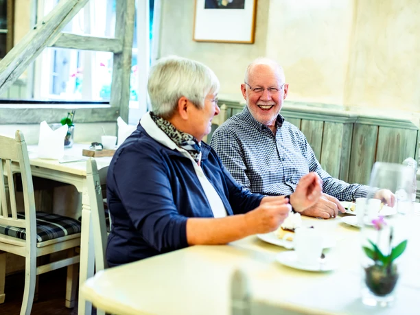 Hotel-Restaurant Wißkirchen Seniorenpaar genießt fröhlich das Frühstück in einem gemütlichen, hellen Café mit ländlichem Flair.