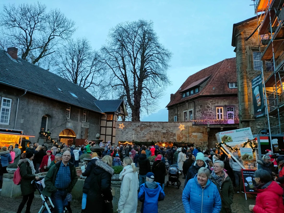 Weihnachtsmarkt Schloss.jpeg Abendlicher Weihnachtsmarkt mit beleuchteten Ständen und Besuchern in historischer Architekturkulisse.
