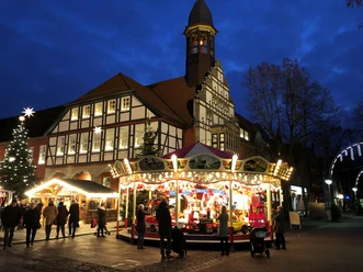 Christmas-lit market square in Nienburg with carousel and half-timbered building at dusk.