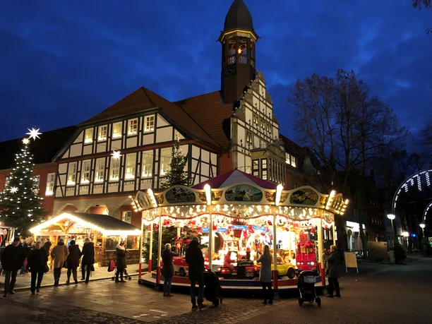 Adventszauber Nienburg (2).jpg Weihnachtlich beleuchteter Marktplatz in Nienburg mit Karussell und Fachwerkgebäude bei Dämmerung.