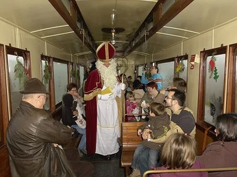 Nikolaus in einem nostalgischen Eisenbahnwaggon, umgeben von fröhlichen Menschen.