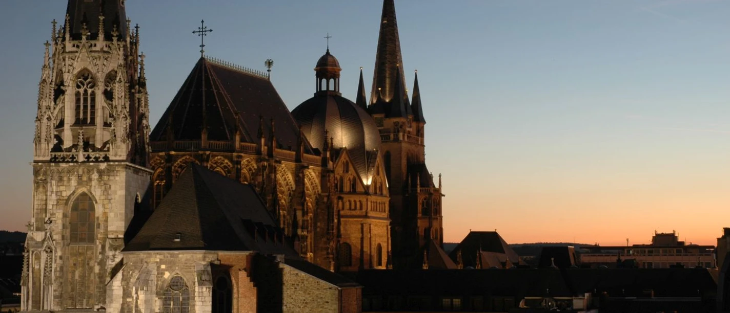 Der beleuchtete Aachener Dom ragt majestätisch in den Abendhimmel.