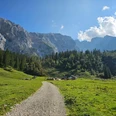 Blick zur Wettersteinalm Schotterweg führt über grüne Almwiese zu einer Hütte vor steilen Felswänden im Sonnenschein