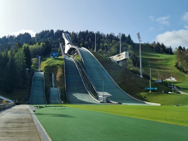 Olympia Skistadion Große Skisprungschanze mit mehreren Anläufen vor bewaldetem Hang unter klarem Himmel
