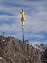Zugspitzkreuz Du siehst ein goldenes Kreuz auf einem Fels mit Schnee.