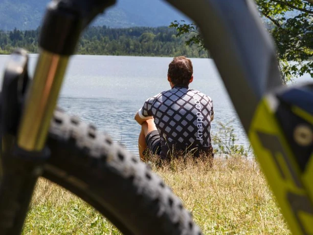 Fahrradfahrer am See Radfahrer sitzt am Seeufer, durch den Rahmen eines Mountainbikes im Vordergrund gesehen.