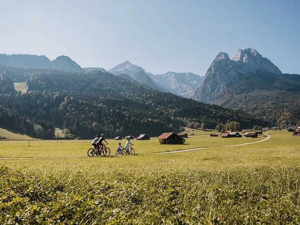 Familie Radl Familie beim Radfahren auf Wiesenweg vor Alpenkulisse mit verstreuten Hütten.