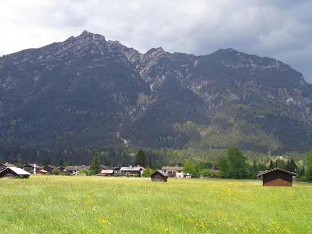 Blick auf den Kramer Weite Blumenwiese mit verstreuten Holzhütten vor einem hohen bewaldeten Bergmassiv