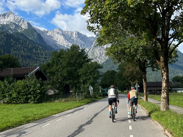 Radweg am Kreuzeck Zwei Radfahrer auf einer Landstraße vor hohen Bergen und grüner Landschaft.