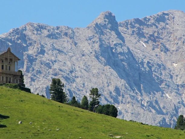 Schachenschloss Schachenhaus auf grüner Anhöhe vor steiler Felswand unter klarem Himmel