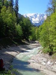 Panorama nach der Partnachklamm Schneebedeckter Gipfel über grünem Wald und hellem Gebirgsbach in einem alpinen Tal