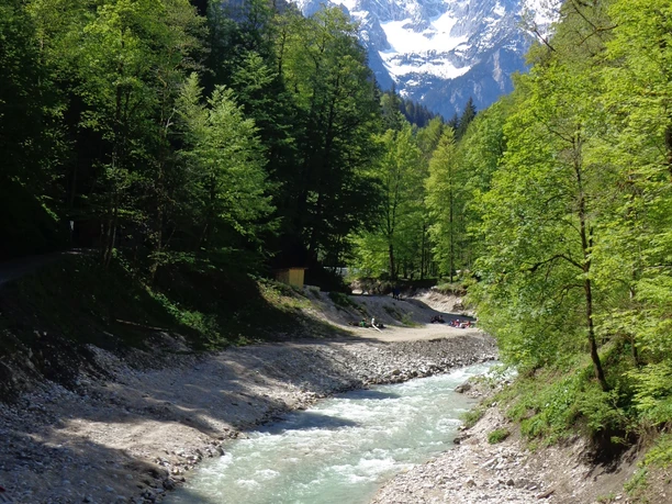 Panorama nach der Partnachklamm Schneebedeckter Gipfel über grünem Wald und hellem Gebirgsbach in einem alpinen Tal