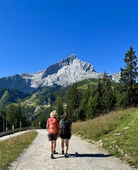 Am Kreuzeck Zwei Wandernde auf breitem Weg vor markanter Felskulisse unter blauem Himmel.
