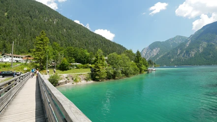 Brücke über den Plansee Holzbrücke über türkisfarbenen See vor bewaldeten Hängen und fernen Bergen bei Sonnenschein
