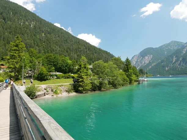 Brücke über den Plansee Holzbrücke über türkisfarbenen See vor bewaldeten Hängen und fernen Bergen bei Sonnenschein