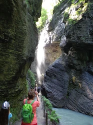 Schmale Klamm mit Wasserfall, Wandernde auf Steg neben türkisfarbenem Bach