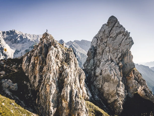 Gatterl Schroffe Felsformationen mit einem wandernden Menschen auf einem Grat vor fernem Alpenpanorama