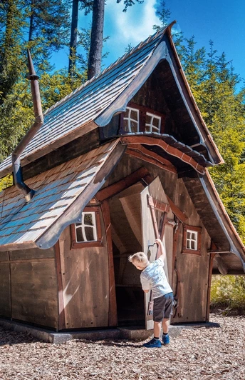 Ein kleiner Junge hat die Tür eines kleinen Holzhauses geöffnet und schaut hinein