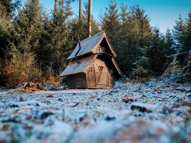 Hexentanzplatz. Ein kleines, schiefes Holzhaus mit weißen Sprossenfenstern und schiefem Kamin steht im Wald