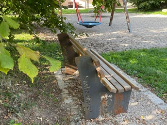 Blick auf Bank am Spielplatz Sasbachried mit Schaukel im Hintergrund.