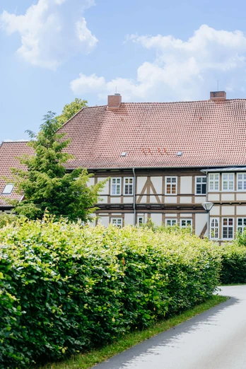 Fachwerkhaus mit rotem Ziegeldach und Laubhecken in einer ländlichen Umgebung, Schlangen, Deutschland.