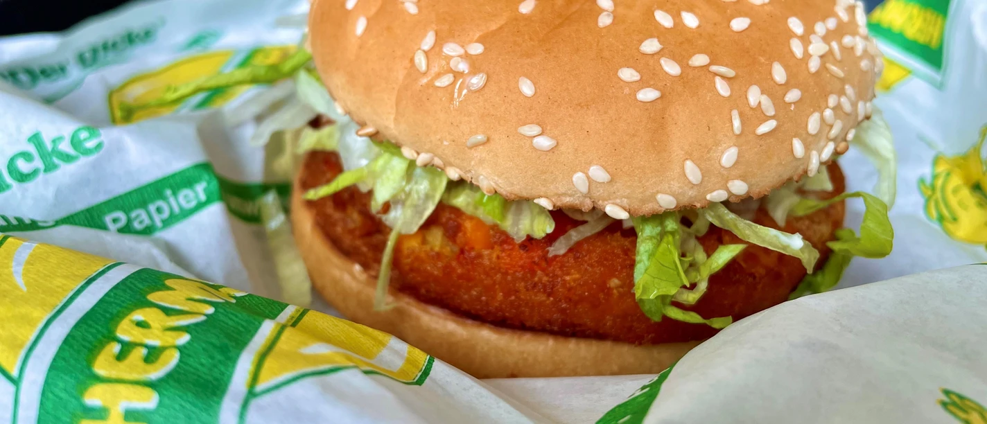 Ein veganes Burgergericht mit einem knusprig panierten Gemüselaibchen und frischem Salat im Sesambrötchen.