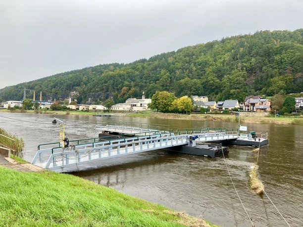 Fähre in Krippen Schwimmende Brücke über einen Fluss, umgeben von Bäumen und Häusern am Ufer.