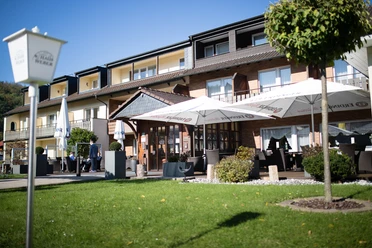Ein dreistöckiges Hotel mit Außenbereich, Sonnenschirmen und Sitzgelegenheiten bei sonnigem Wetter.