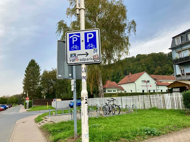 A street sign points to a bicycle parking lot, a German Red Cross building and a green landscape can be seen in the background.