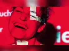 Eine Person lacht herzlich vor einem intensiv rot beleuchteten Hintergrund mit Textfragmenten.