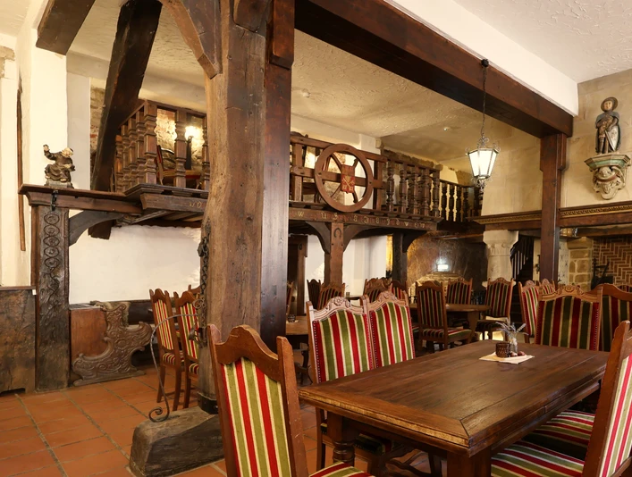 schloss_petershagen_gorgonius_2864a.jpg Rustikaler Gastraum mit Holztischen und Stühlen, dekorativen Holzbalken und ausdrucksvollen Wandverzierungen.