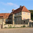 schloss_petershagen_vorhof_2647a.jpg Schloss Petershagen mit rotem Ziegeldach, umgeben von Bäumen und einem geräumigen Vorhof.