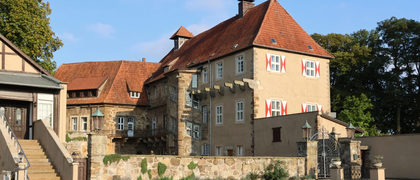 schloss_petershagen_vorhof_2647a.jpg Schloss Petershagen mit rotem Ziegeldach, umgeben von Bäumen und einem geräumigen Vorhof.