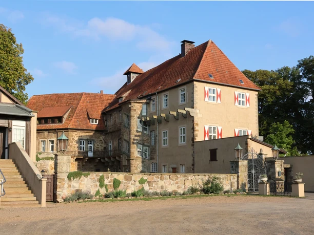 schloss_petershagen_vorhof_2647a.jpg Schloss Petershagen mit rotem Ziegeldach, umgeben von Bäumen und einem geräumigen Vorhof.