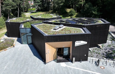 Modernes, polygonales Gebäude mit begrüntem Dach und der Aufschrift "Klima Erlebniswelt".