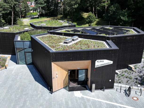 Modernes, polygonales Gebäude mit begrüntem Dach und der Aufschrift "Klima Erlebniswelt".