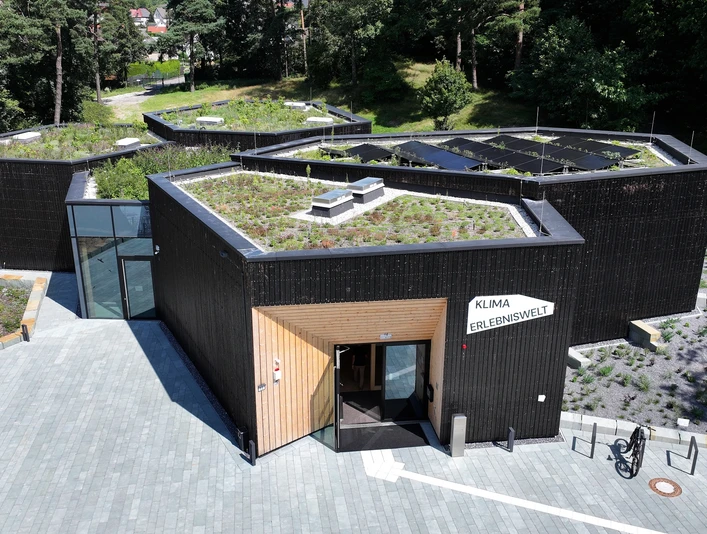 Modernes, polygonales Gebäude mit begrüntem Dach und der Aufschrift "Klima Erlebniswelt".