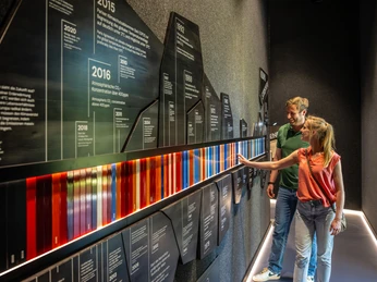 KEW_198©LTM GmbH, D.Ketz.jpg Zwei Personen betrachten interaktive Informationstafeln in einem modernen Museumsraum.