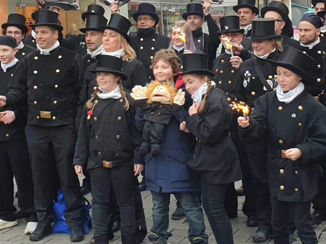 Schornsteinfeger_Umzug_Pro Herford GmbH.jpeg Eine Gruppe von Schornsteinfegern steht zusammen, alle sind lächelnd und tragen traditionelle Uniformen.