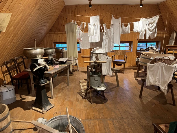Historische Waschküche mit Holzwänden, Geräten, Wäscheleinen, alten Waschmaschinen und Wannen.
