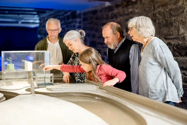 Wasserkraft im Aggertal Fünf Personen, darunter ein Kind, betrachten gemeinsam ein Wassermodell in einem Museumsraum.