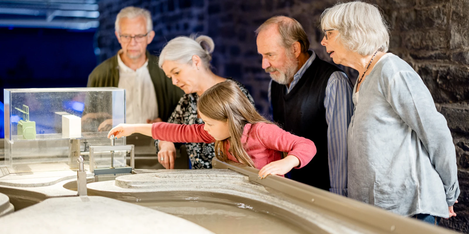 Wasserkraft im Aggertal Fünf Personen, darunter ein Kind, betrachten gemeinsam ein Wassermodell in einem Museumsraum.