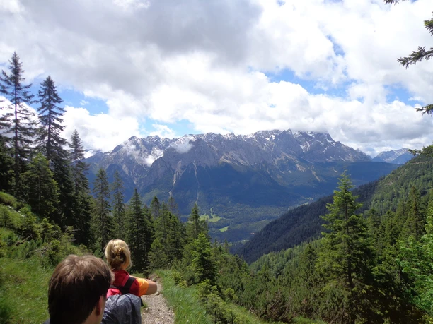Steig zur Stepbergalm Wandernde auf Bergpfad vor bewaldeten Hängen und schneebedeckten Gipfeln unter Wolken