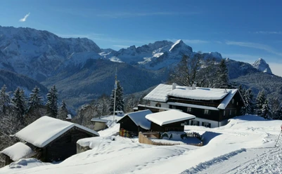 Gasthof Eckbauer Verschneite Berghütten vor hohen Gipfeln unter klarem Himmel.