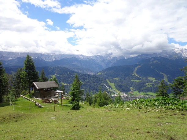Hütte auf einer Wiese Berghütte auf grüner Alm mit weitem Blick auf bewaldete Hänge und wolkenverhangene Berge